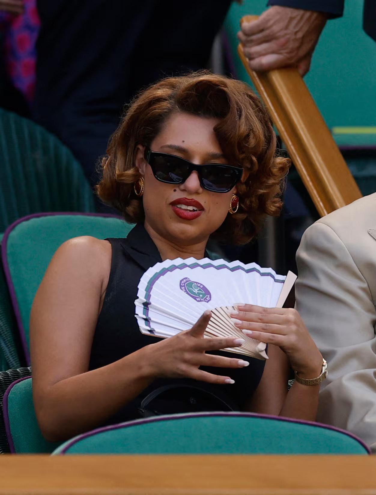 Raye destaca con negro sin mangas, labios rojos, aros dorados y un abanico blanco con el logo de Wimbledon