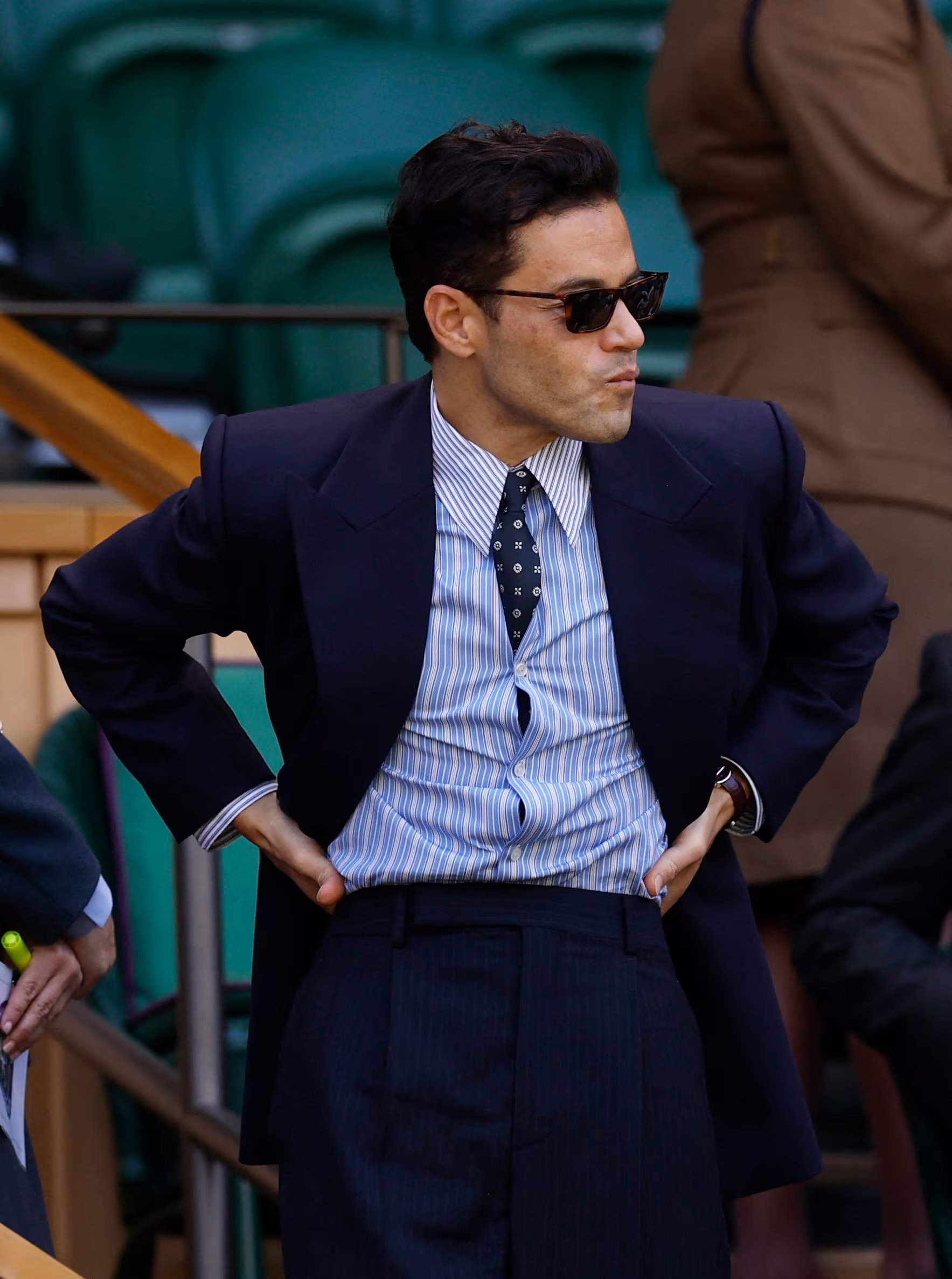 Rami Malek elige sastrería azul marino con camisa a rayas, corbata de motivos y gafas oscuras para un aire clásico