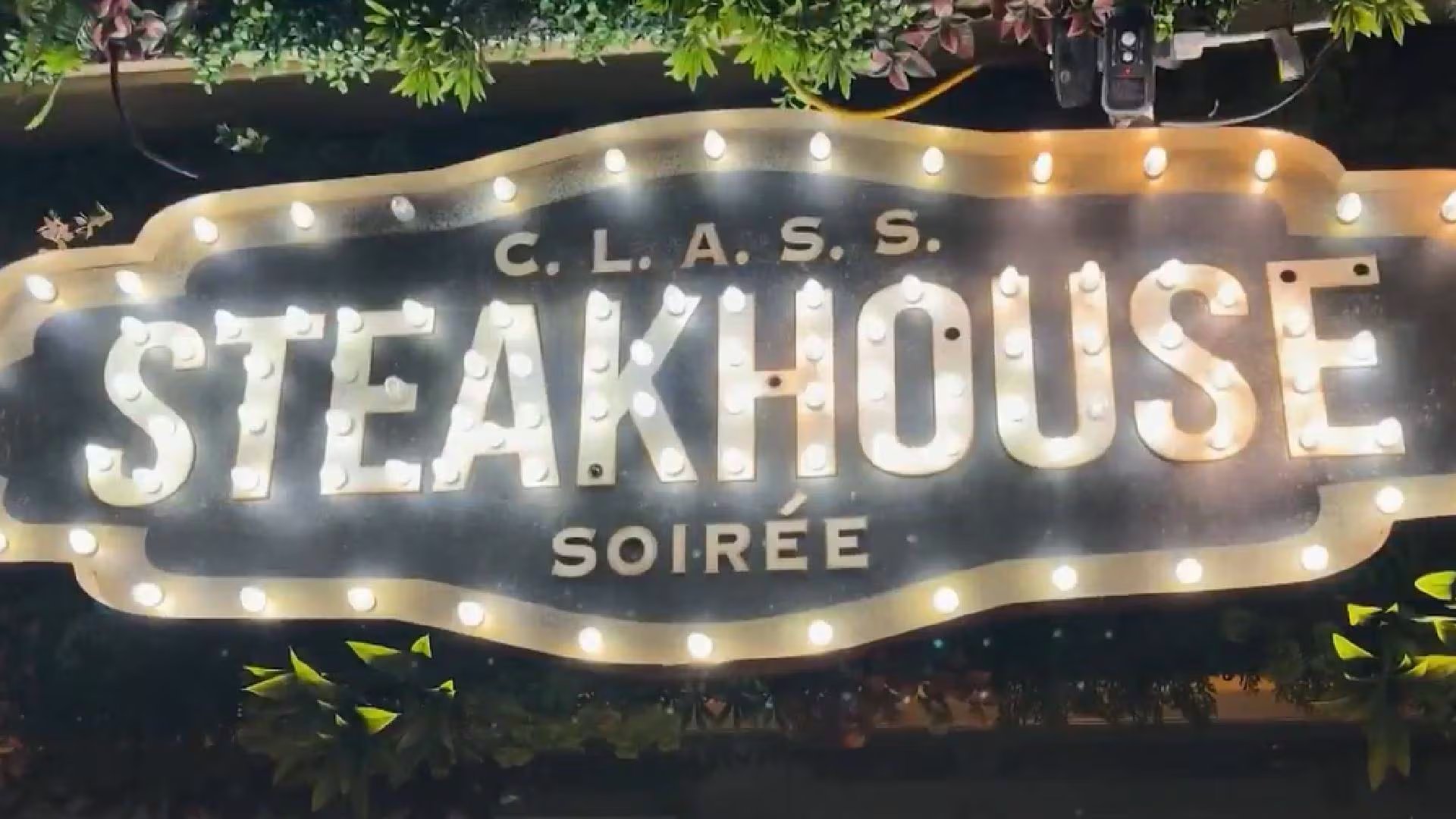 Un letrero luminoso con las palabras C. L. A. S. S. STEAKHOUSE SOIRÉE ilumina un área rodeada de vegetación (NBC)