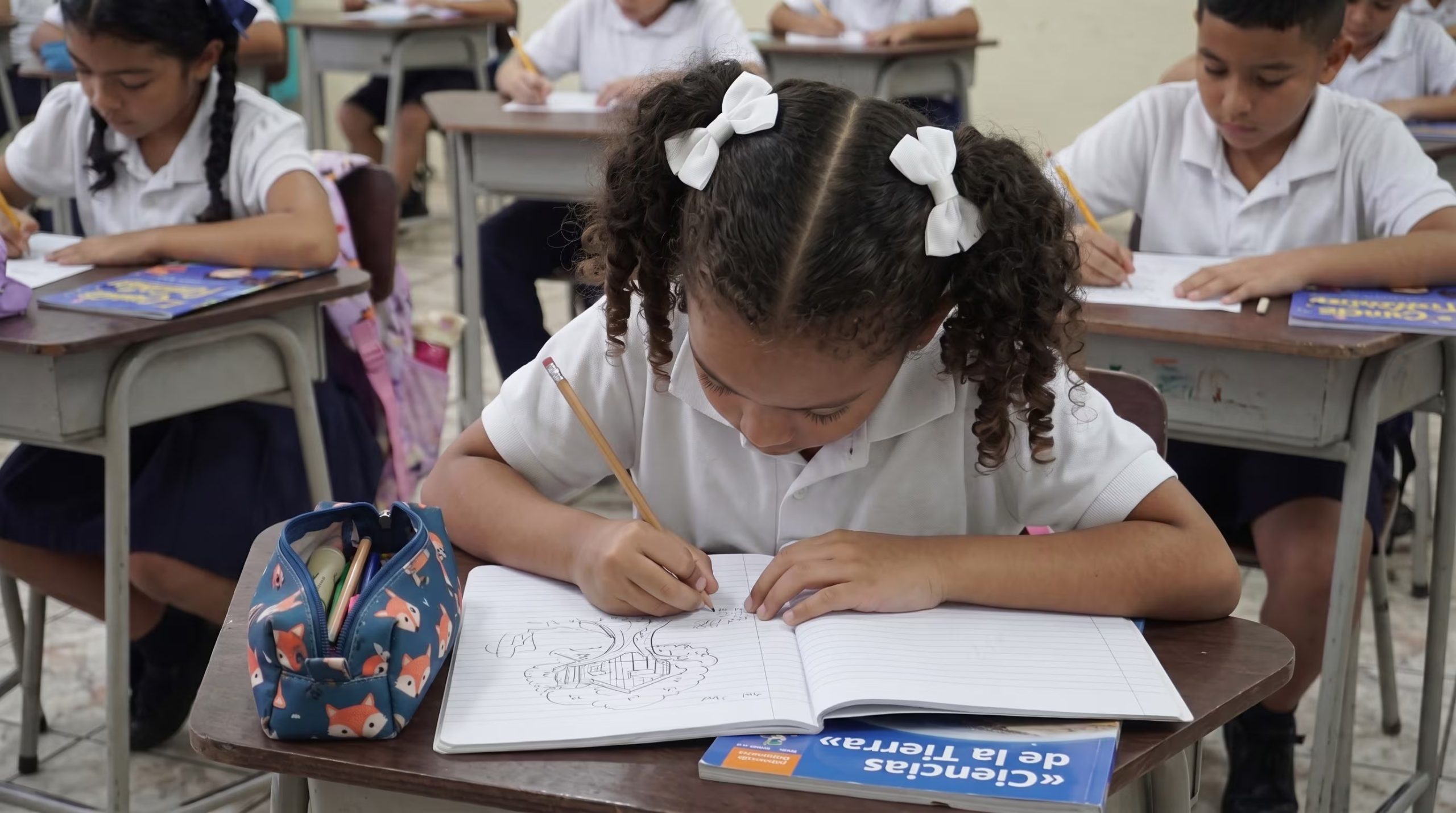Una estudiante escribe en su cuaderno escolar junto a sus compañeros dentro de un salón de clases. (Imagen Ilustrativa Infobae)