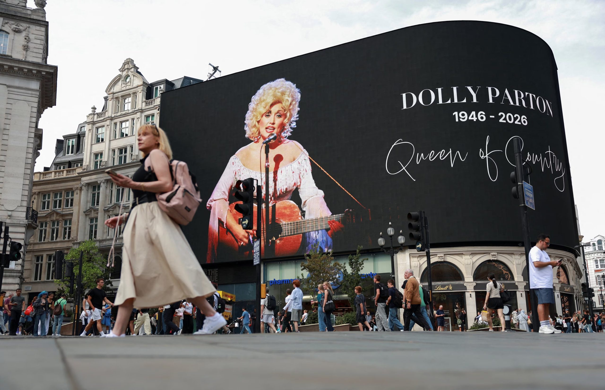 People walk past a tribute to U.S. country singer Dolly Parton at Piccadilly Circus, a day after the announcement of her death at age 80, in London, Britain, August 26, 2026. REUTERS/Hiba Kola