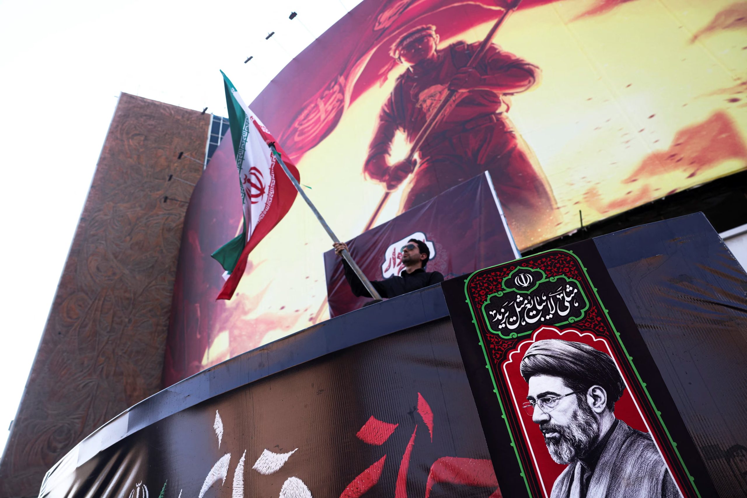 Un hombre sostiene una bandera iraní junto a una fotografía del líder supremo de Irán, Mojtaba Khamenei, en Teherán (Majid Asgaripour/WANA vía REUTERS)
