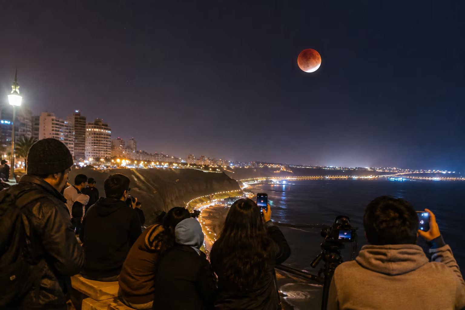 Varias personas observan y fotografían un eclipse lunar sobre la costa de Lima, Perú, durante la noche del 27 de agosto. (VisualesIA)