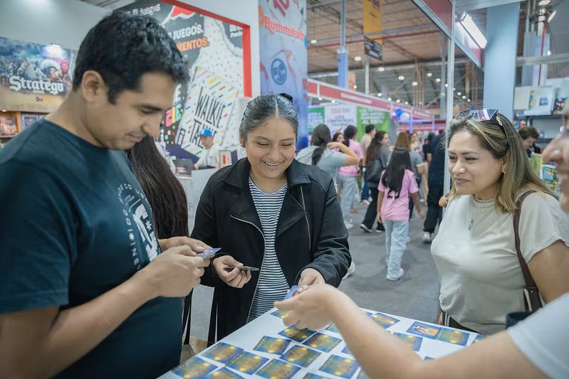 Visitantes de la Feria Internacional del Libro de Lima 2026 observan y manipulan tarjetas de juegos en un stand del evento.