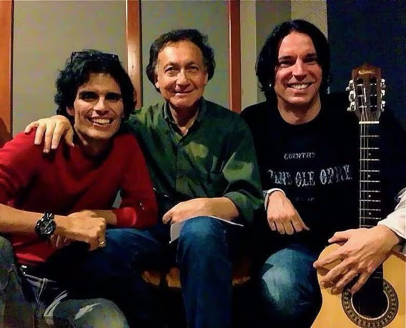 Guillermo Bussinger posa sonriente junto a otros dos músicos en un estudio de grabación, uno de ellos con una guitarra acústica.
