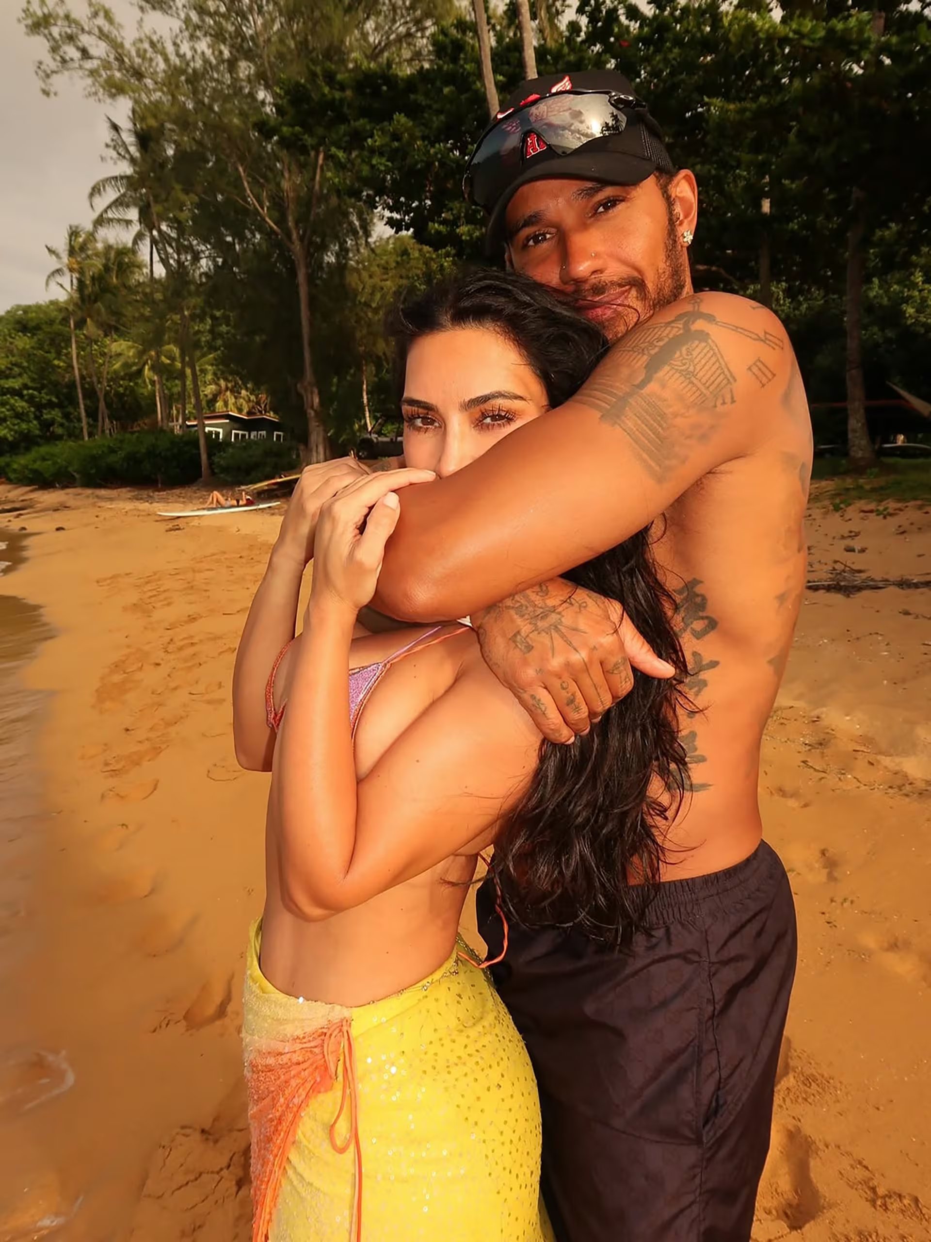 Kim Kardashian y Lewis Hamilton se abrazan en la orilla de una playa tropical, con palmeras, en sus vacaciones