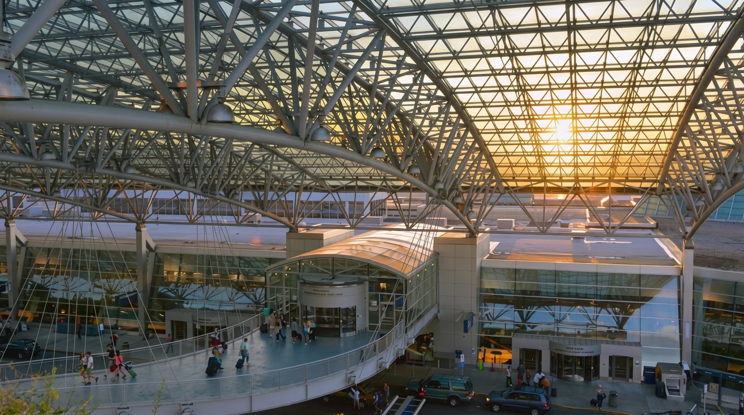 Varias personas caminan con maletas por una pasarela peatonal de la terminal de un aeropuerto cubierta por una estructura metálica. (Imagen Ilustrativa Infobae)