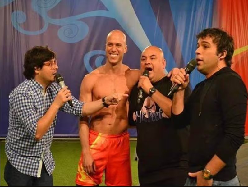 El locutor Mr. Peet, con otros tres hombres en un escenario, considera volver a ser la voz de Combate.