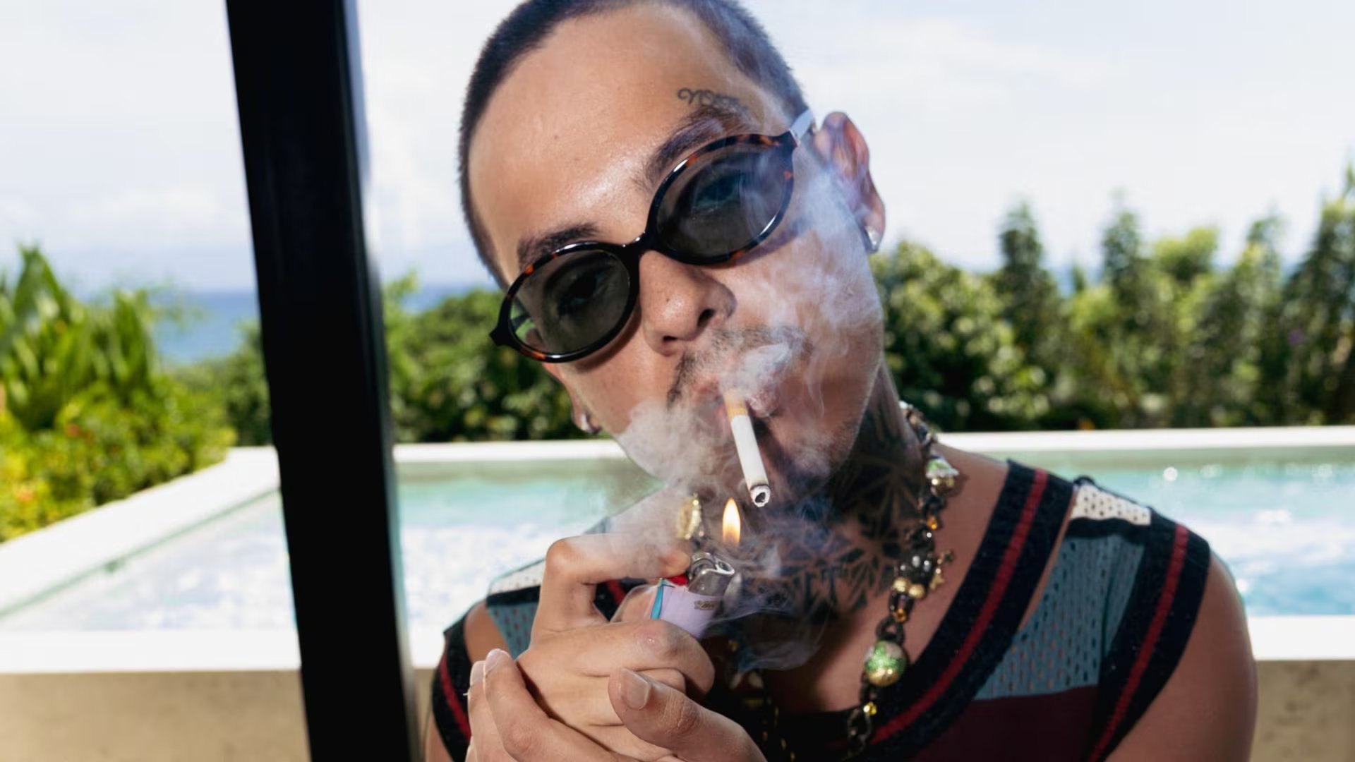 El cantante mexicano Natanael Cano enciende un cigarrillo frente a una piscina al aire libre. (Instagram: Natanael Cano)