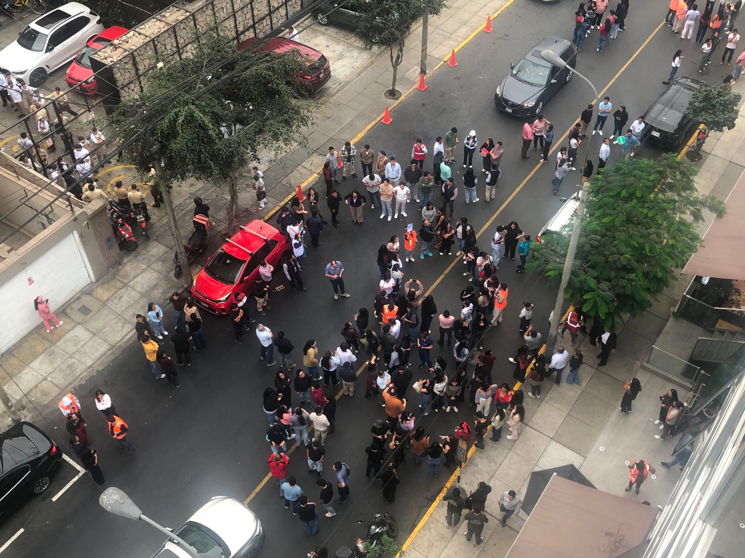 Trabajadores de oficinas y locales comerciales de Miraflores, Lima, evacúan a la calle durante el Simulacro Nacional Multipeligro, mientras vehículos detienen su marcha. (Infobae / Valeria Mendoza)