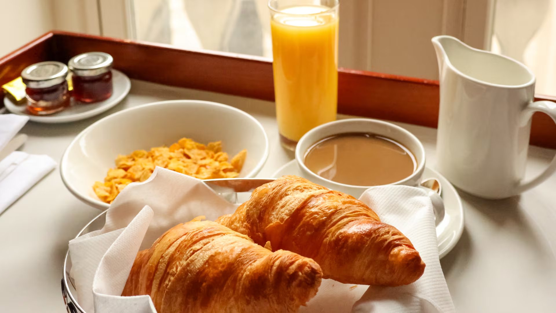 Un desayuno con zumo, café, cereales y croissants (Canva)