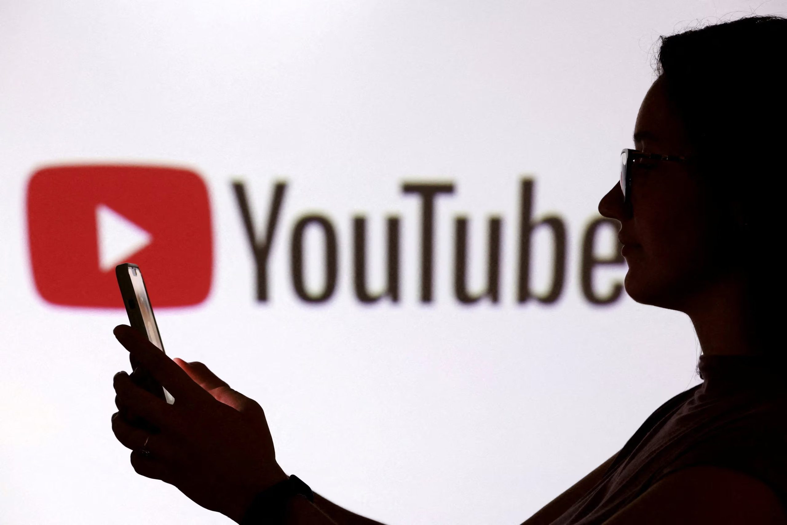 FILE PHOTO: A teenager poses for a photo while holding a smartphone in front of a Youtube logo in this illustration taken September 11, 2025. REUTERS/Dado Ruvic/Illustration/File Photo