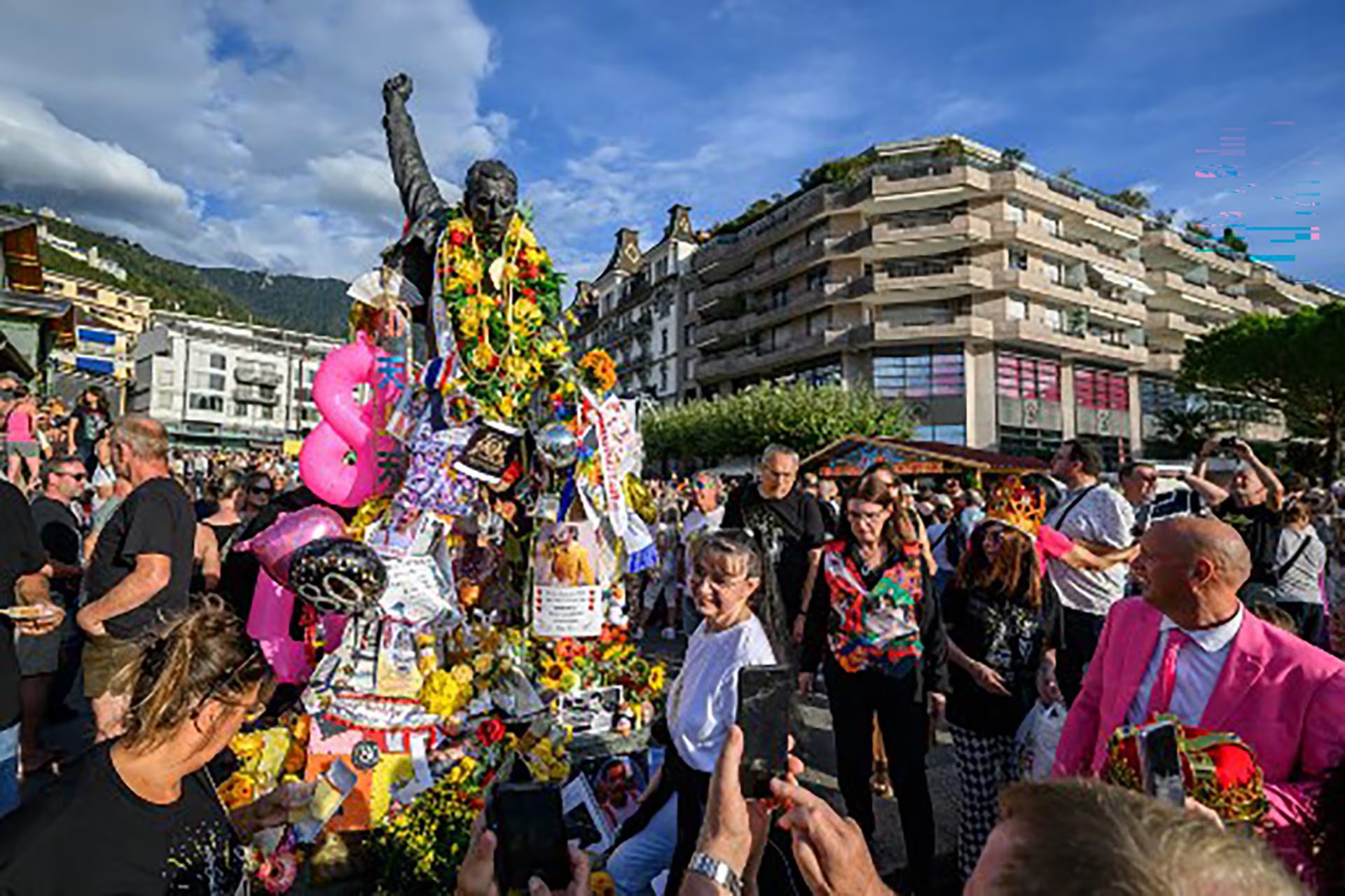 Varias personas se congregan junto a la estatua de Freddie Mercury, decorada con arreglos florales y globos para conmemorar el aniversario de su nacimiento.