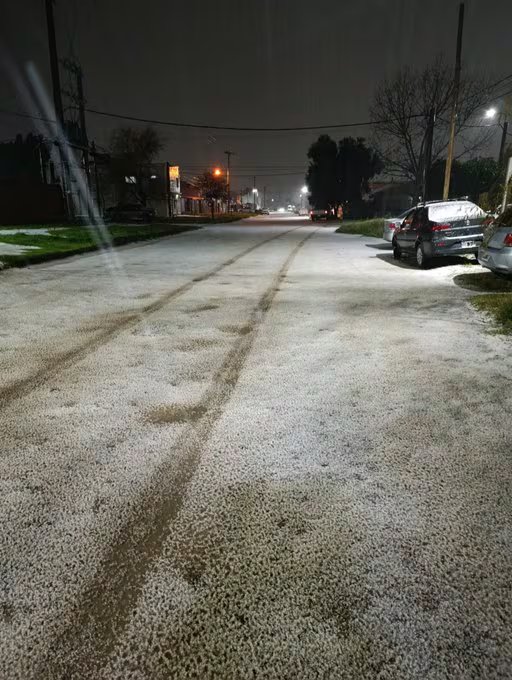 Una calle residencial permanece cubierta por una capa de granizo durante la noche mientras las marcas de neumáticos atraviesan la calzada.