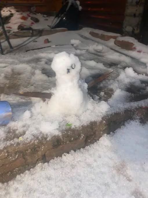 Una pequeña figura elaborada con graupel permanece sobre un murete de ladrillo cubierto de hielo tras el paso de una tormenta invernal.
