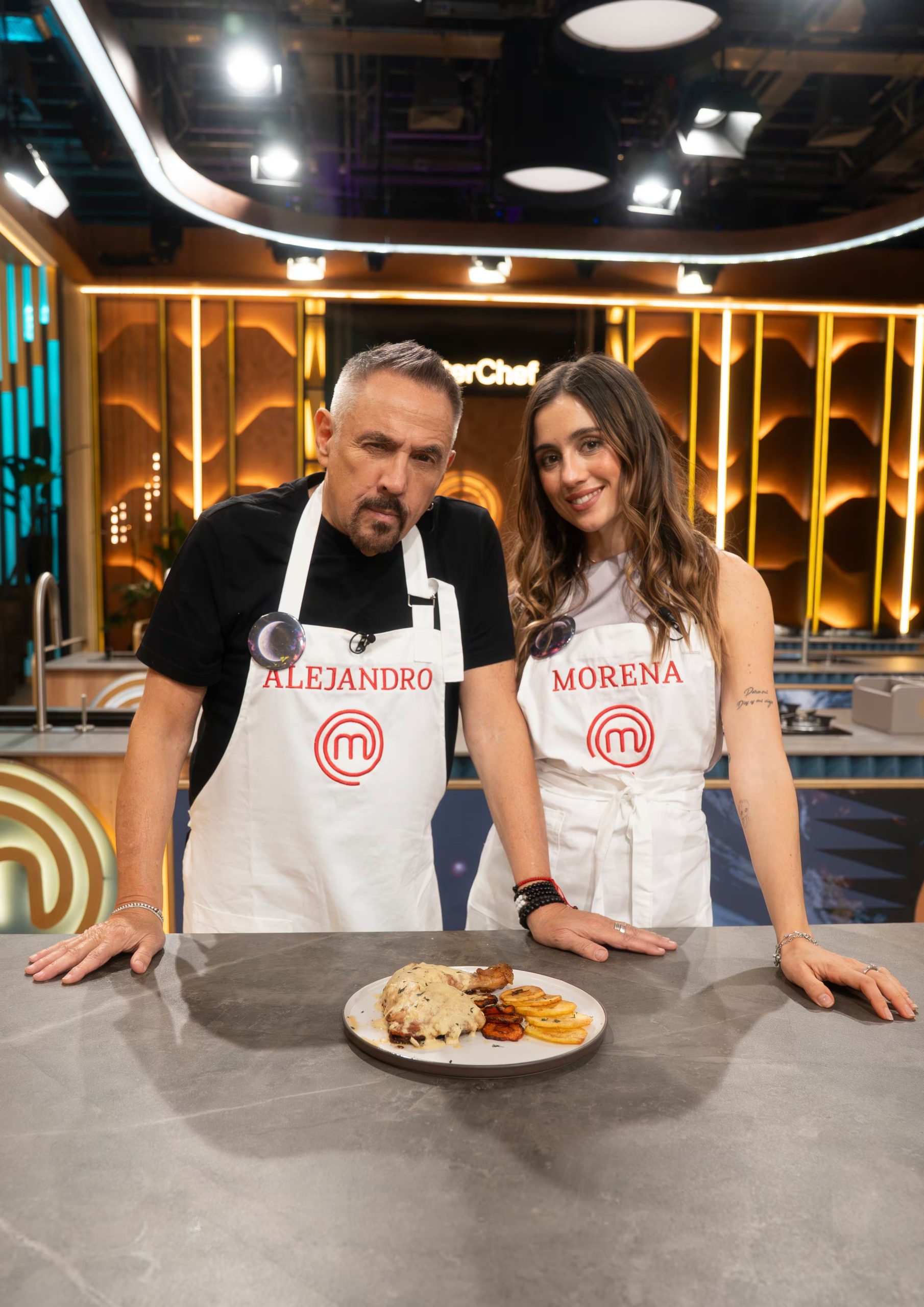 Alejandro Lerner y Morena Beltrán posan junto a un plato preparado en el estudio de televisión de MasterChef Celebrity.