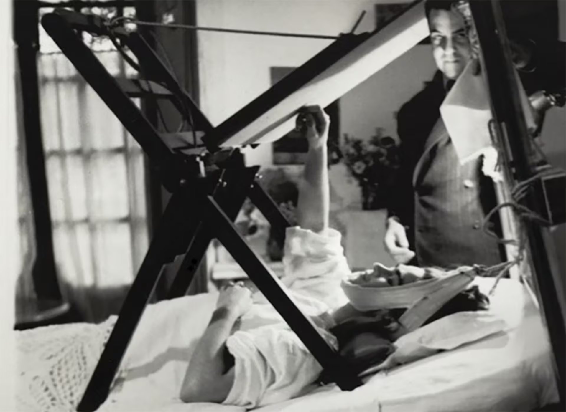Frida Kahlo pinta recostada en su cama mediante una estructura de madera adaptada a sus necesidades de reposo luego del grave accidente. En la foto aparece Diego Rivera