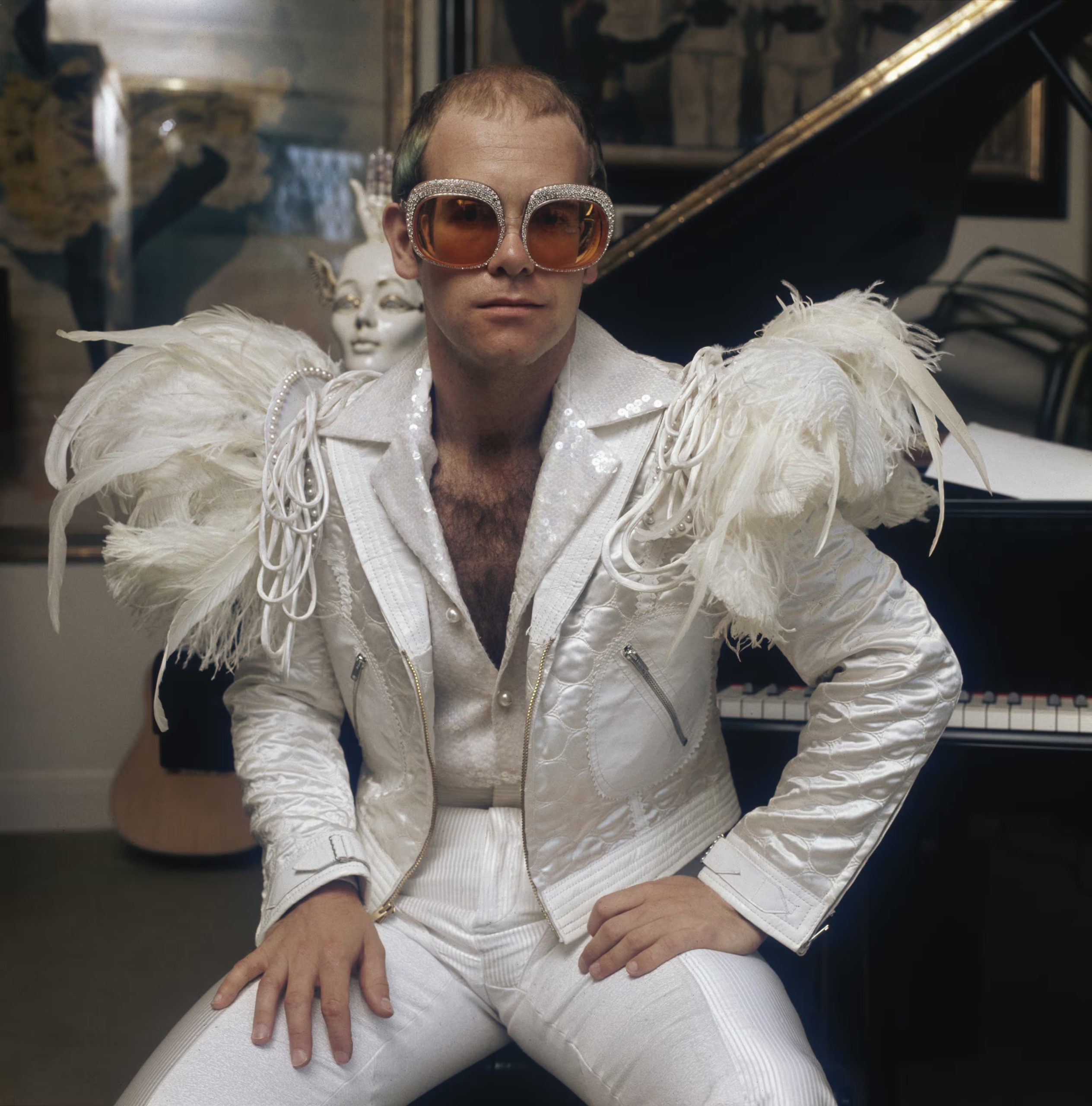 English pop singer Elton John in a flamboyant stage outfit of white suit with feather trim and rhinestone encrusted glasses, circa 1973.
