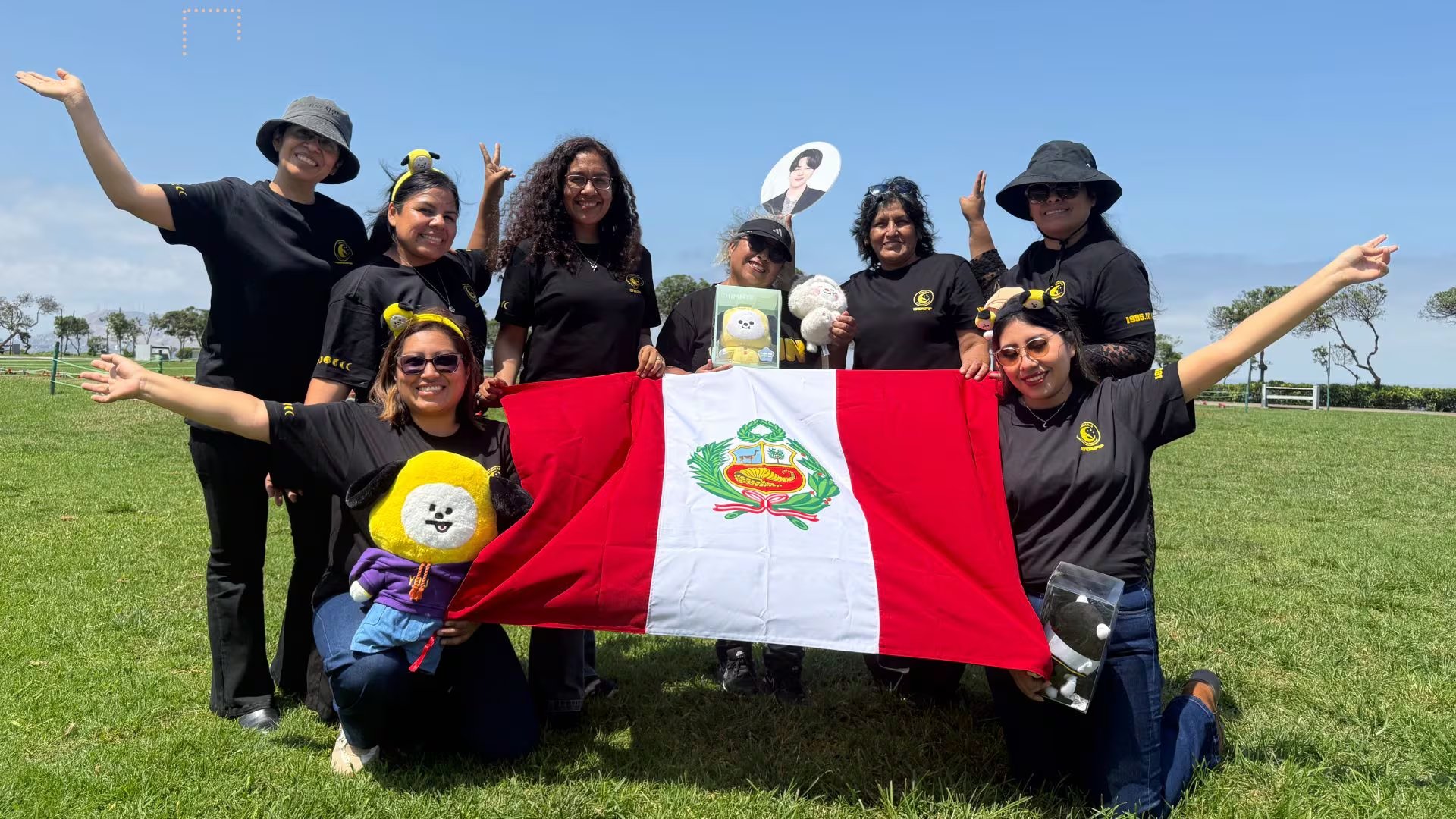 Integrantes del club de fans de Jimin, PJmusas, posan al aire libre con camisetas negras, artículos temáticos del cantante y la bandera de Perú. (Paula Arias)