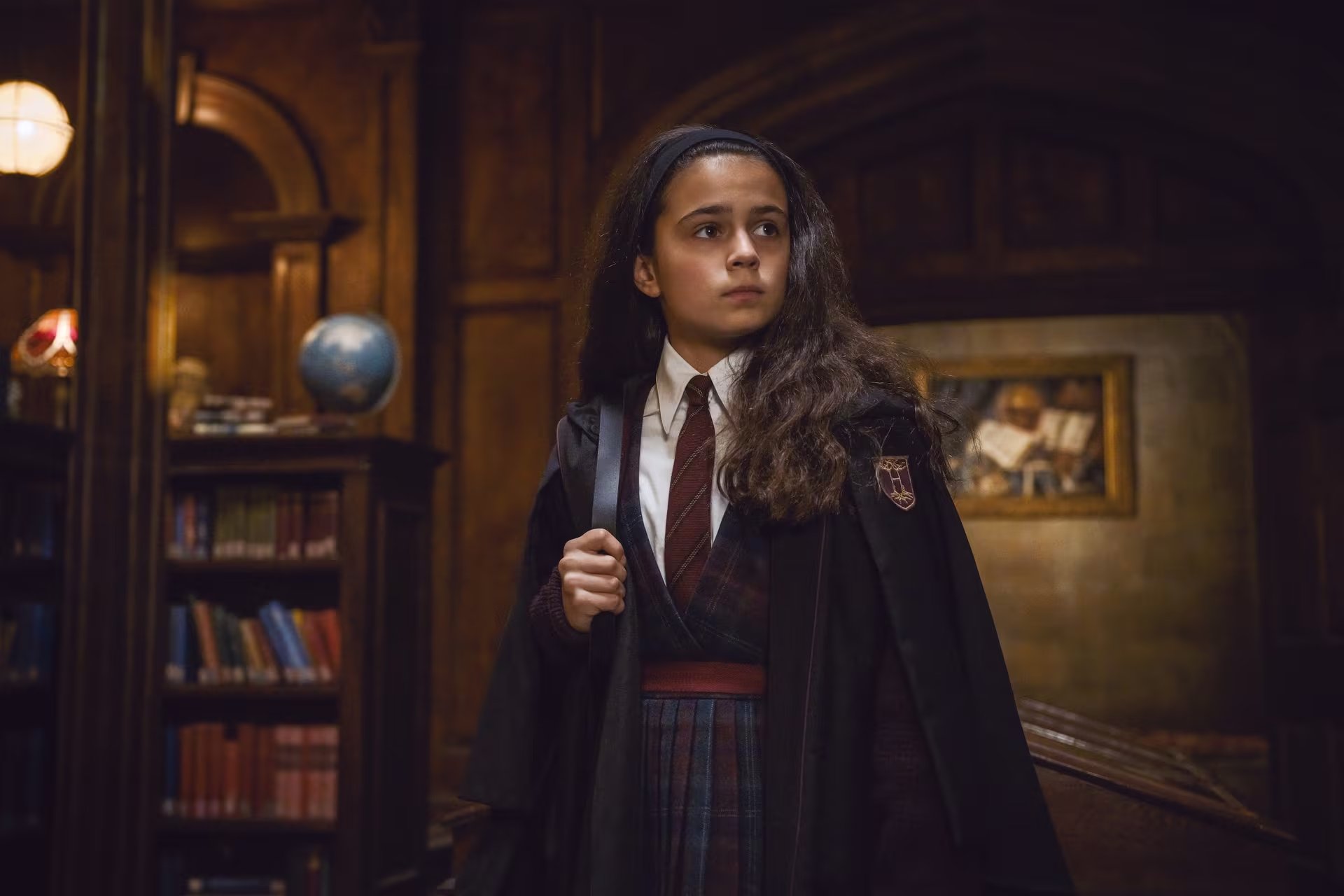 Arabella Stanton viste el uniforme escolar y la túnica del personaje Hermione Granger en un escenario de estilo académico. (HBO Max)