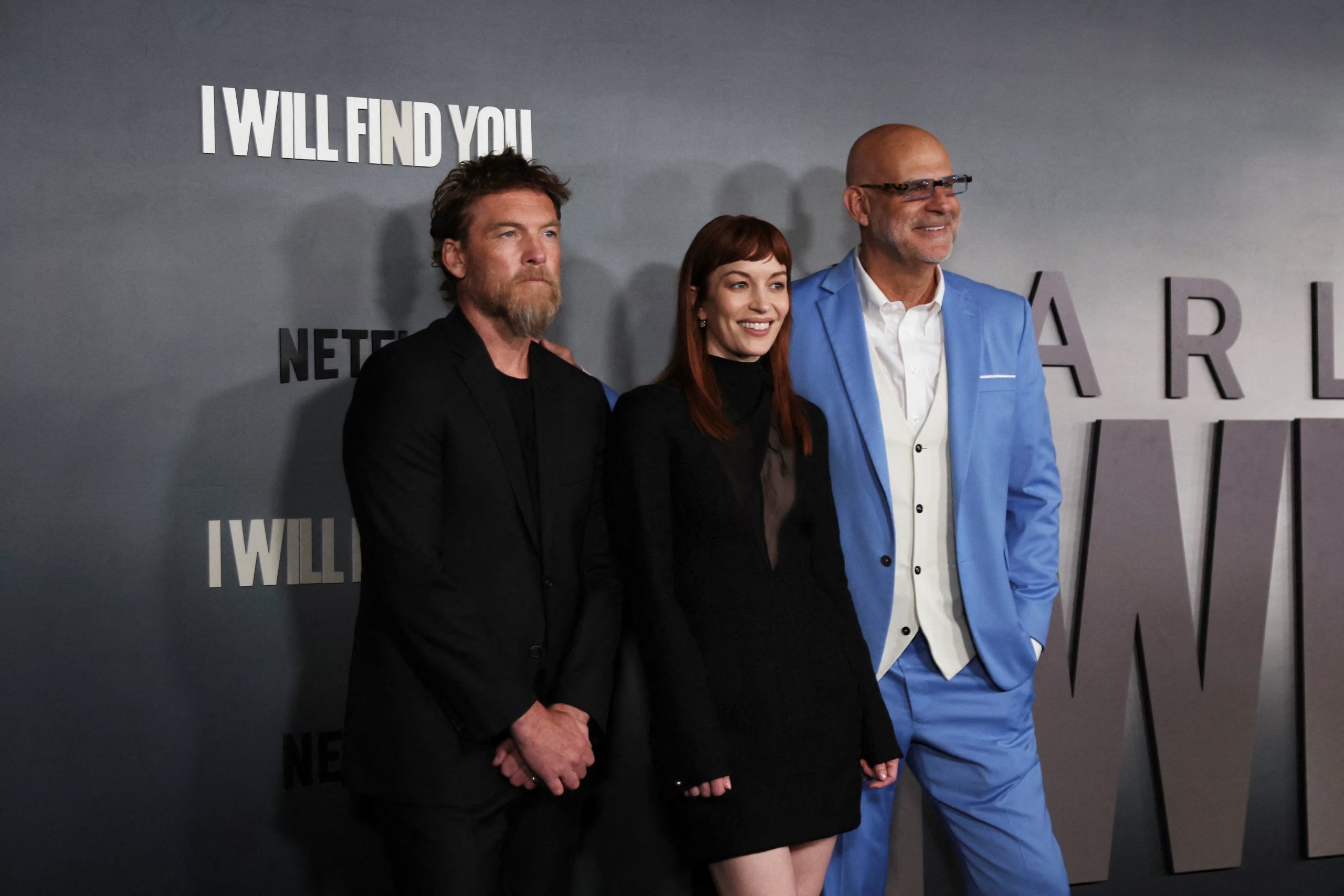 Sam Worthington, Britt Lower y Harlan Coben posan juntos en la alfombra roja durante el estreno de la producción de Netflix