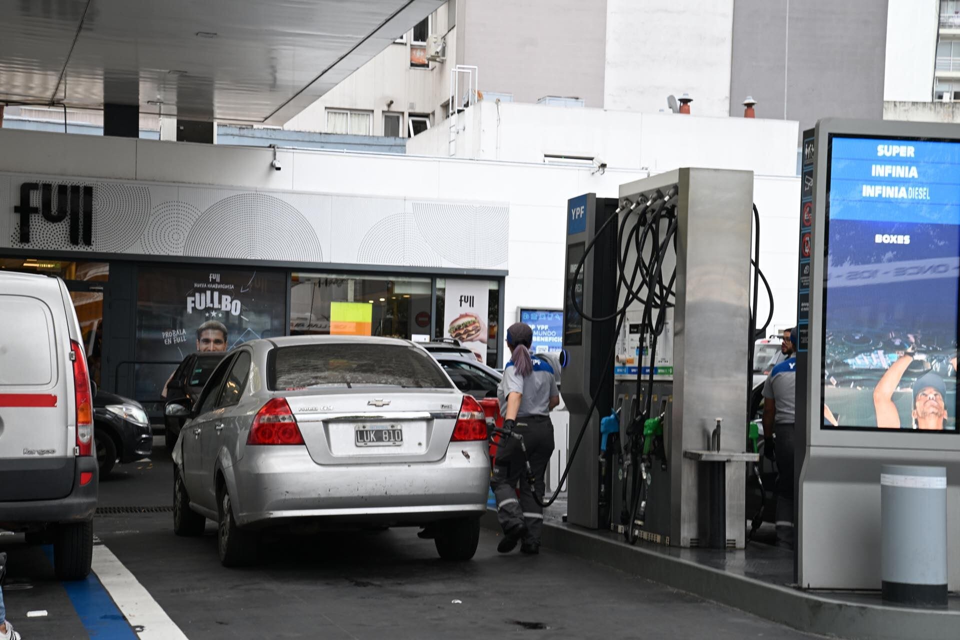 Automóviles y un empleado de YPF en una estación de servicio durante el proceso de abastecimiento de combustible, con los precios y tipos visibles en un panel digital. (Maximiliano Luna)