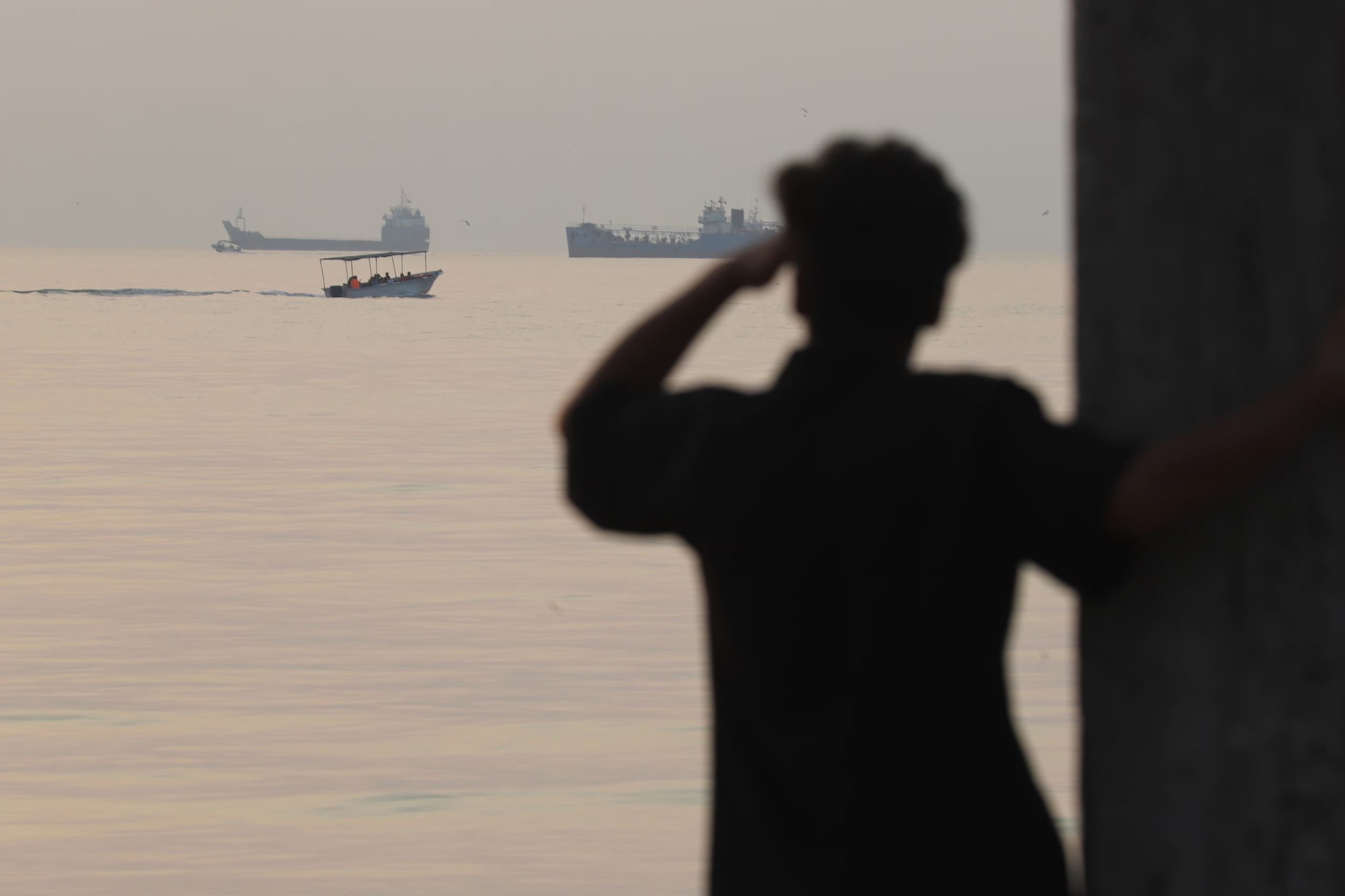 Un hombre observa el mar mientras una pequeña embarcación pasa frente a buques de carga anclados en el estrecho de Ormuz, el sábado 24 de octubre de 2026, en Bandar Abbas, Irán. (Amirhosein Khorgooi/ISNA via AP)