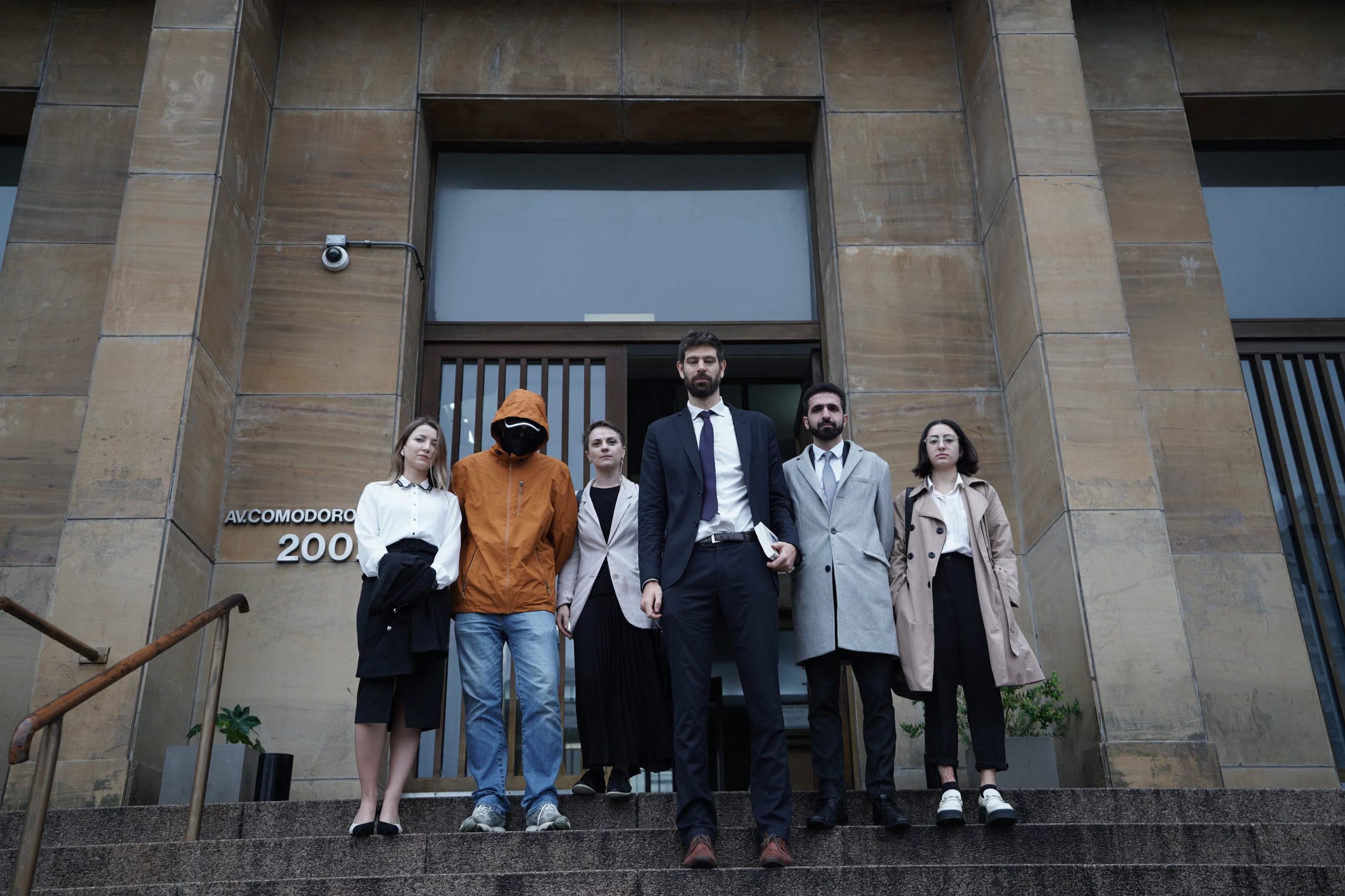 Integrantes de The Reckoning Project y sus abogados, entre ellos Marcos Aldazabal, frente a Comodoro Py durante la presentación de la denuncia, en 2024. Chebaevskyi, con el rostro cubierto, había pedido que se resguardara su identidad: en el expediente figura como «V.1». (Foto: The Reckoning Project para Infobae.)