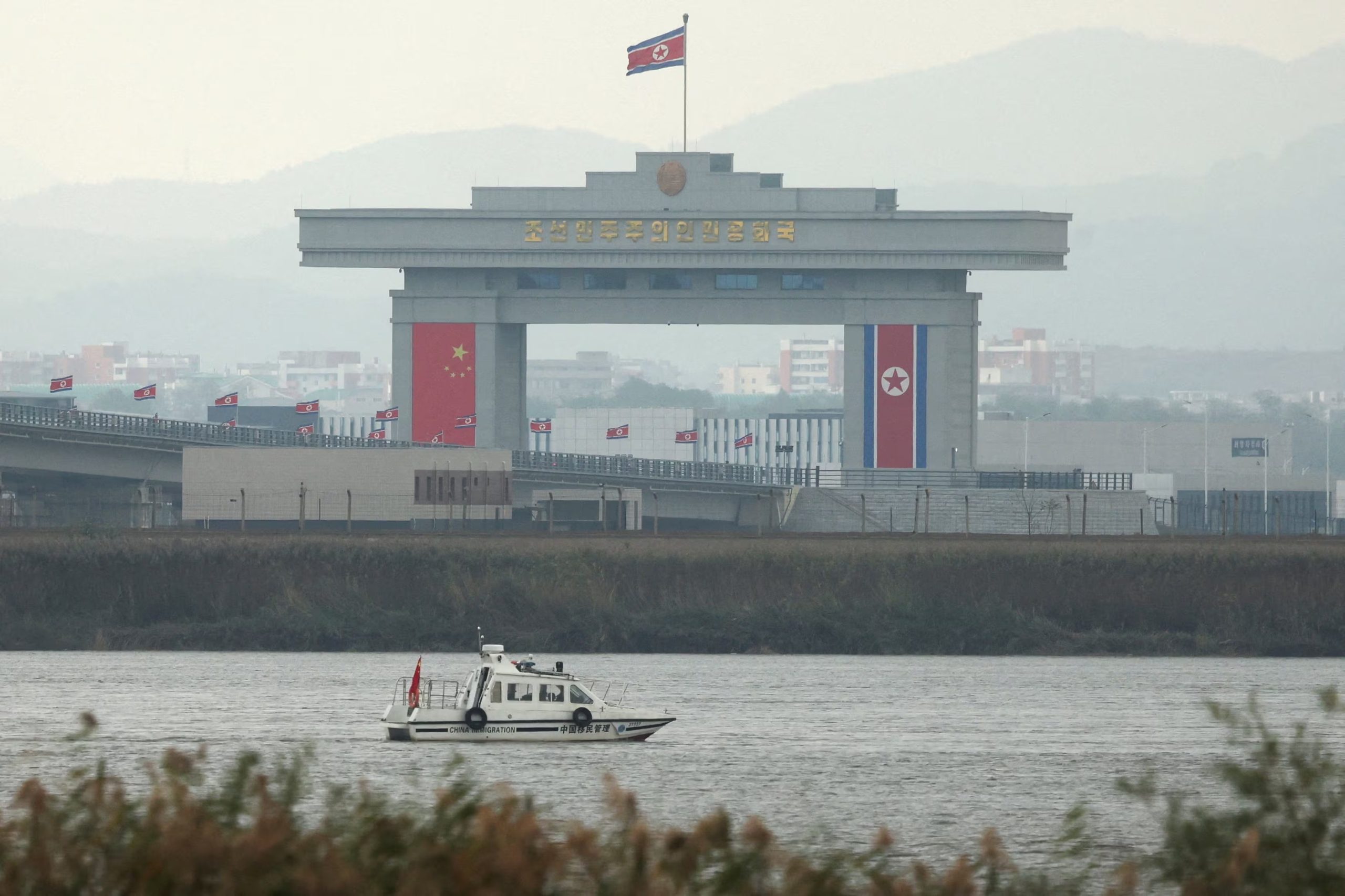 Una embarcación de inspección migratoria de China navega por el río Yalu, pasando junto a un edificio de aduanas norcoreano situado en el extremo del recién inaugurado Nuevo Puente del Río Yalu —que conecta Sinuiju, en Corea del Norte, con la Nueva Zona de Dandong, en China—, tal como se observa desde Dandong, en la provincia de Liaoning, China, el 15 de octubre de 2026 (REUTERS/Florence Lo)