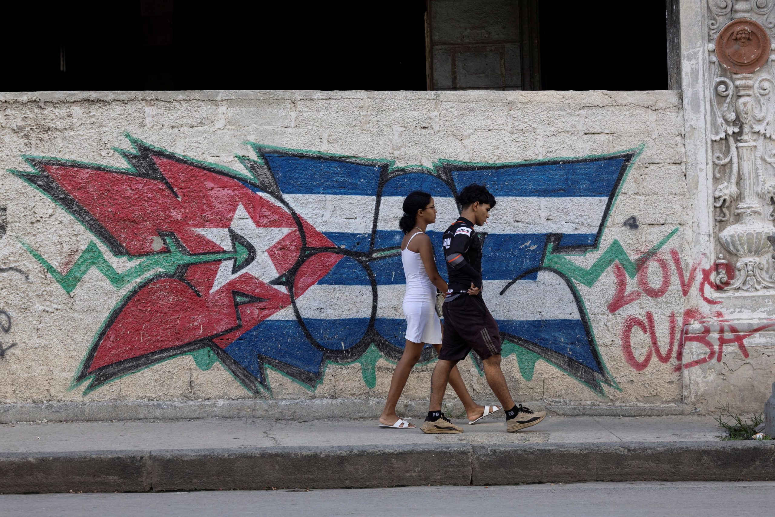 Una mujer y un hombre caminan junto a un grafiti con los colores de la bandera cubana en La Habana, Cuba. 4 de octubre de 2026. REUTERS/Ricardo Arduengo