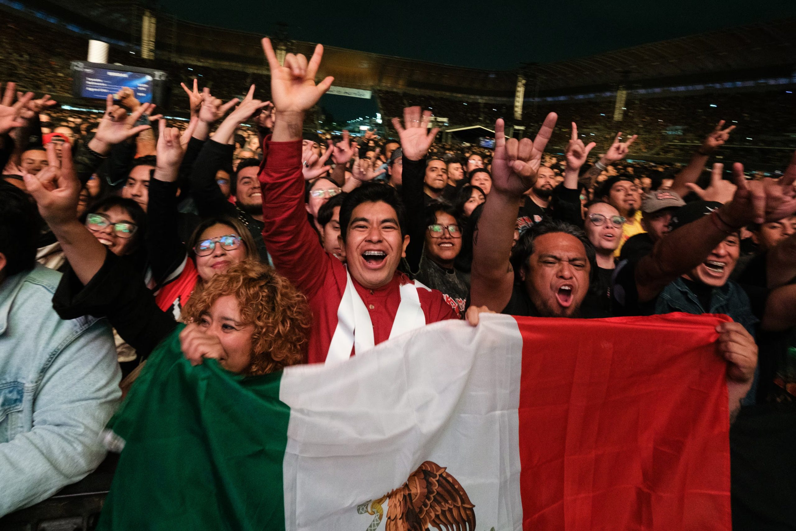 Un grupo de asistentes sostiene la bandera de México y levanta las manos durante un concierto masivo realizado en un estadio. (Liliana Estrada/Cortesía OCESA)