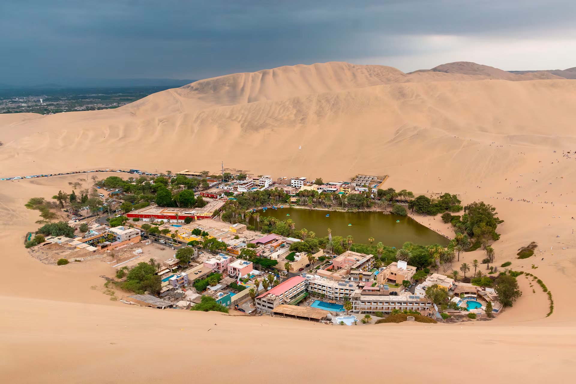 El oasis de la Huacachina se ubica entre dunas de arena con una laguna central y edificaciones alrededor. (Pexels)